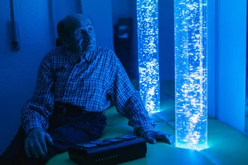 Elderly man relaxing in sensory room with bubble tubes