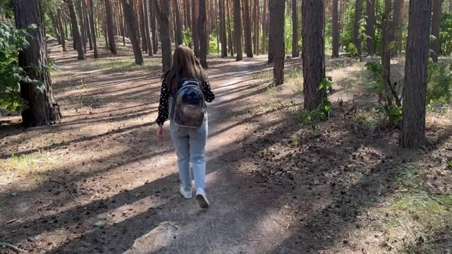 Woman walks with cat in carrier through forest path