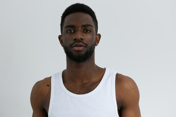 Confident man in casual white tank top stands against a plain white background, gazing directly at the camera