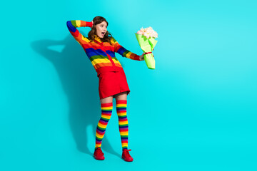 Cheerful woman with rainbow-themed outfit and flowers against a teal background expressing joy and...