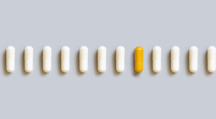 Beige medical capsules in a line with yellow one in the middle on grey top view. Dietary supplements