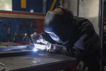 Skilled craftsman with a protective helmet and safety gear, carefully welding together metal pieces...