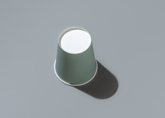 Disposable light green paper cup on a grey with hard shadow top view , mockup. Sustainable lifestyle