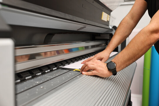Man using wide-format printer indoors, closeup. Printing house