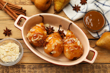 Delicious pears with caramel sauce, almond flakes and spices on wooden table, top view
