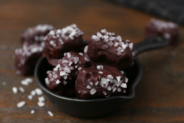 Tasty chocolate candies with salt in bowl on wooden table, closeup