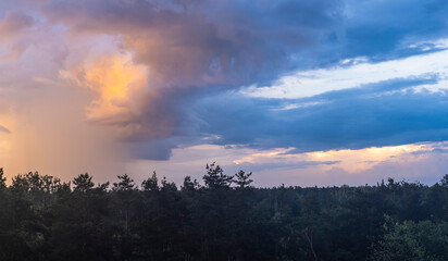 Colorful sunset illuminating clouds over a dense forest landscape during late evening hours