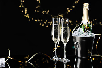 Champagne and bucket of ice on mirror surface against black background with blurred lights, space for text