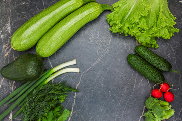 Vegetables, root vegetables and herbs lie against a background of dark marble around the edges with space for text in the center. The concept of cooking, proper nutrition, diet, and detox. High