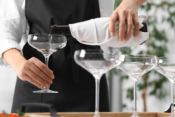 Waiter filling glasses with champagne indoors, closeup
