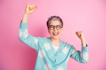 Cheerful mature woman celebrating success, wearing floral cardigan against pink background