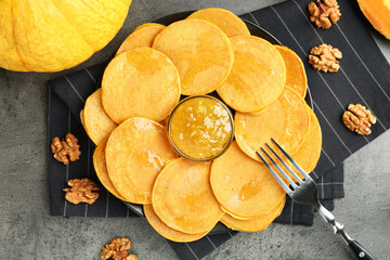 Tasty pumpkin pancakes with walnuts and jam on grey table, flat lay