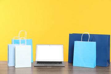Internet shopping. Laptop and colorful paper bags on wooden table against yellow background
