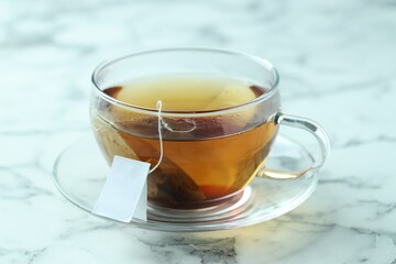 Tea bag in glass cup with hot drink on light marble table, closeup