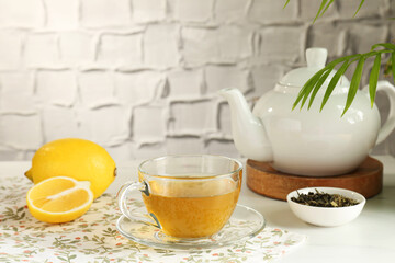 Refreshing green tea in cup, lemon and dry leaves on white table against textured wall