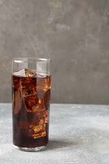 Refreshing cola with ice cubes in glass on light textured table against grey background, closeup....