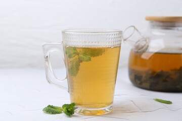 Aromatic mint tea and fresh leaves on white textured table, closeup