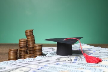 Graduate hat, dollar banknotes and coins on wooden table, closeup. Tuition payment