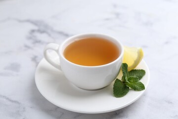 Aromatic mint tea in cup, fresh leaves and lemon on light marble table, closeup