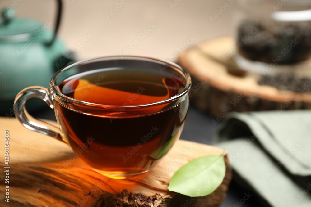 Wall mural Aromatic black tea in cup and green leaf on wooden snag, closeup