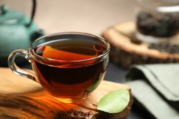 Aromatic black tea in cup and green leaf on wooden snag, closeup