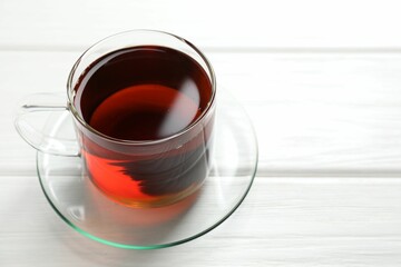 Aromatic black tea in cup on white wooden table, closeup. Space for text