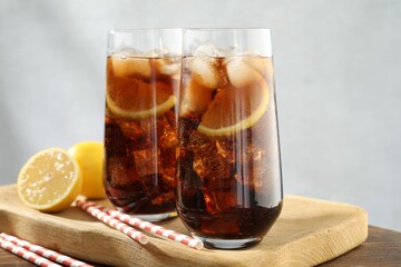 Refreshing iced cola with lemon slices on wooden table, closeup