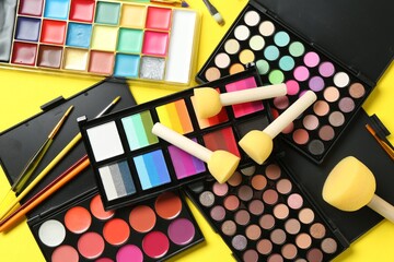 Face paints, tools and makeup products on yellow background, flat lay
