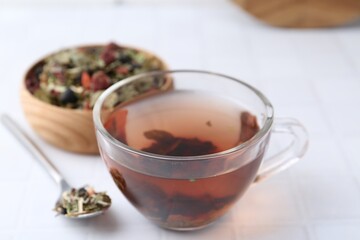 Delicious herbal tea and dry leaves on white tiled table, closeup