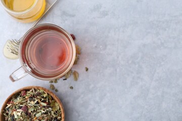 Delicious herbal tea with honey and dry leaves on grey table, flat lay. Space for text