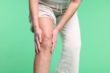 Woman suffering from pain in her knee on green background, closeup