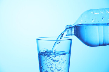 Pouring soda water from bottle into glass on light blue background, closeup. Space for text