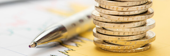 Ein Stapel Euromünzen und Kugelschreiber liegt auf einem Chart mit Finanzen