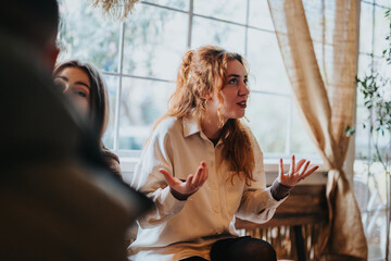 Young woman passionately gestures and speaks during a conversation in a beautifully lit cafe.