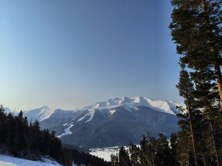 Snow-covered mountains rise majestically above a serene landscape under a clear blue sky in winter