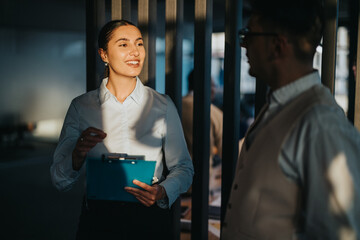 A confident businesswoman engages in conversation with a colleague in a modern office setting,...