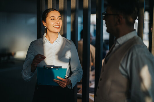 A confident businesswoman engages in conversation with a colleague in a modern office setting, symbolizing teamwork and professional collaboration. The warm lighting adds a welcoming atmosphere.