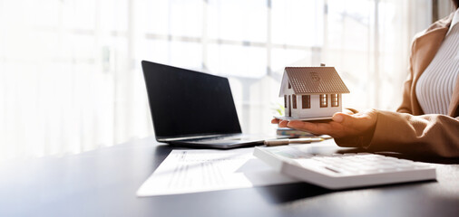 Fototapeta premium Female woman hand holding home model, investment small miniature white toy house. Mortgage property insurance dream moving home and real estate concept