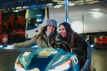 Two friends share a joyful moment driving a bumper car at a festive winter event, capturing...