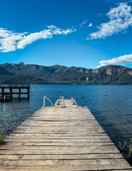 Fototapeta premium Wooden pier leading into a blue lake with mountains