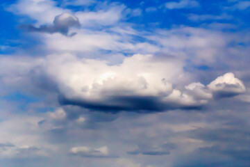 Fluffy clouds scattered across vibrant blue sky, creating peaceful and tranquil atmosphere under natural sunlight with various shapes and shades of clouds noticeable. Selective focus, defocus