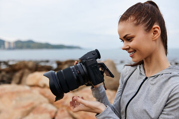 Young woman admiring her professional camera with a smile, dressed in a gray hoodie, set against a...
