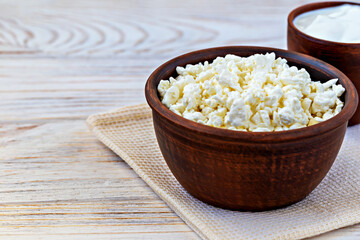 Dairy products. Bowl of fresh cottage cheese displayed in rustic clay serving dish placed on soft cloth on wooden tabletop. Concept of healthy eating and culinary recipes. Rural dairy products
