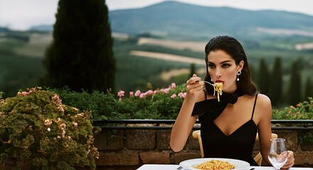 Italian cuisine, hospitality concept. Beautiful young woman in classic black dress eating pasta in restaurant. Great Tuscany view. Banner style. Outdoor shot