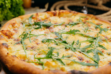 Gourmet four-cheese pizza with arugula, served on a wooden board in a stylish restaurant setting