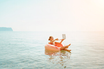 Woman laptop sea. Freelancer woman in sunglases floating on an inflatable big pink donut with a laptop in the sea. People summer vacation rest lifestyle concept