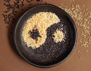 Yin-Yan symbol spelled by two kind of raw rice. Black and white rice on the plate. Brown rice and black rice in symbol of yin yan. 