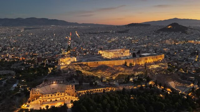 Aerial view of Parthenon in Athens, Greece before sunrise. Acropolis is illuminated with city lights, ancient theater sitting below. Fly over Parthenon in Athens - famous Greek tourist attraction
