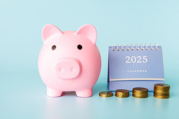 A piggy bank in the form of a pink pig, a desktop calendar for 2025 and stacks of coins on a light background. The concept of financial accumulation.