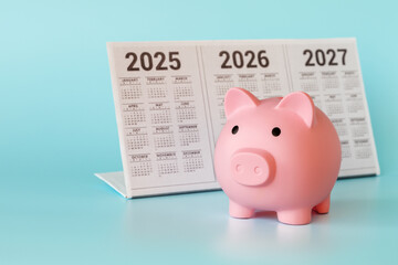 A piggy bank in the form of a pink piglet and a desktop calendar for 2025-2027 on a light blue background. The concept of long-term investments.